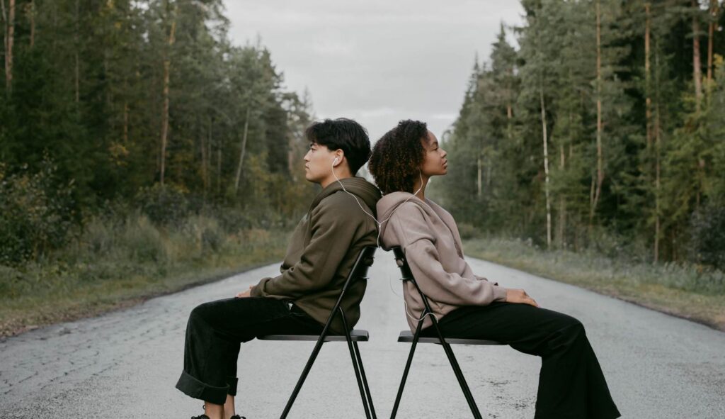 a couple sitting in chairs in the middle of a forest road listening to music while facing away from each other - yes this is a strange photo
